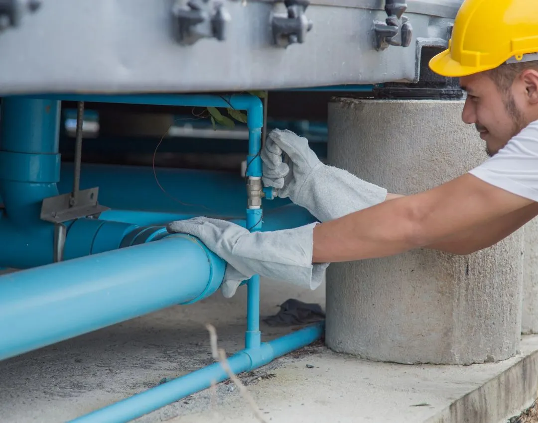 A professional plumber in a blue cap fixing a kitchen sink drainage system in a Columbia, SC home.