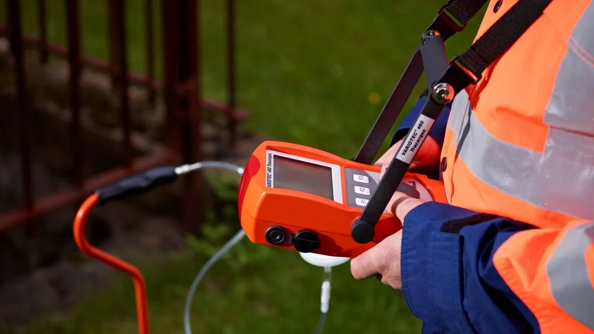 A specialized technician in an orange safety vest using a Variotec 460 tracer gas device for non-invasive leak detection in a Columbia, SC yard.