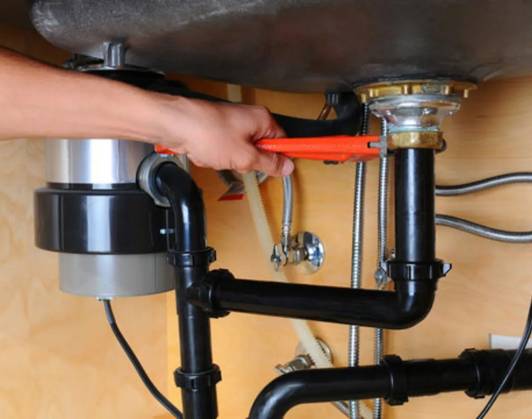 A plumber using a red pipe wrench to install and secure a new kitchen garbage disposal unit under a sink in a Columbia, SC home.