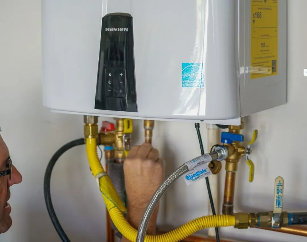A professional plumber installing a Navien tankless water heater in a Columbia, SC home, focusing on gas and water line connections.