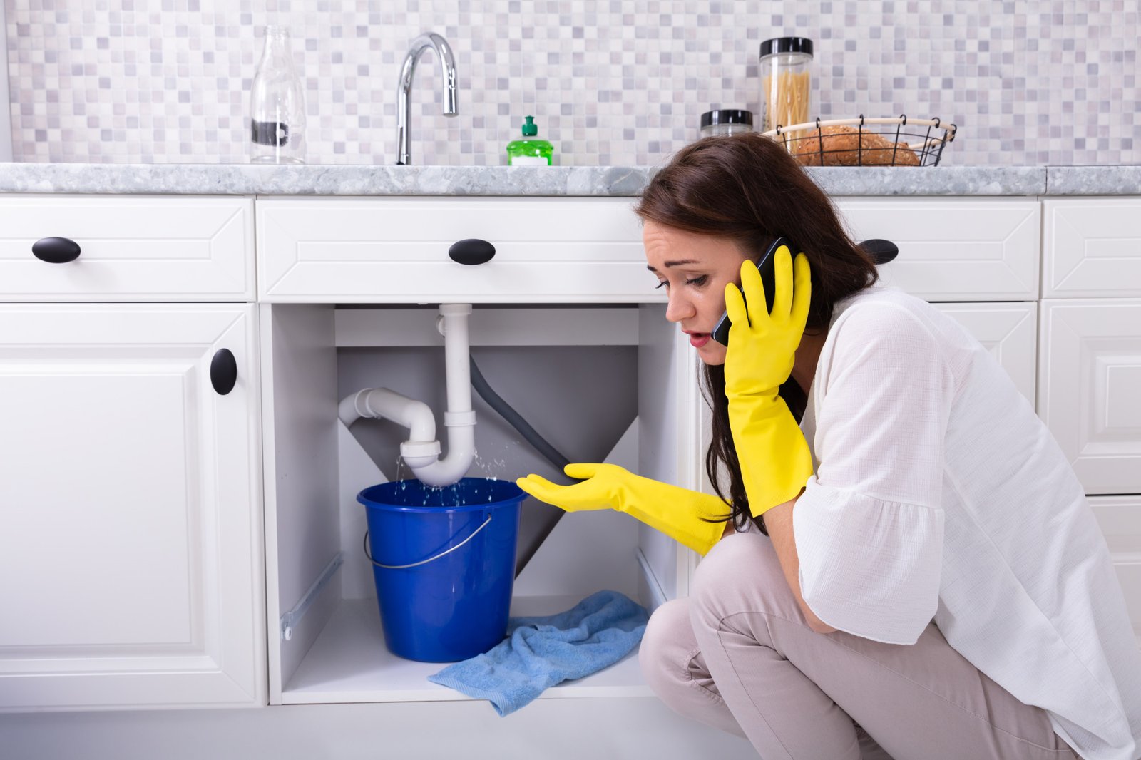 Woman Calling Plumber In Front Of Water Leaking From Pipe
